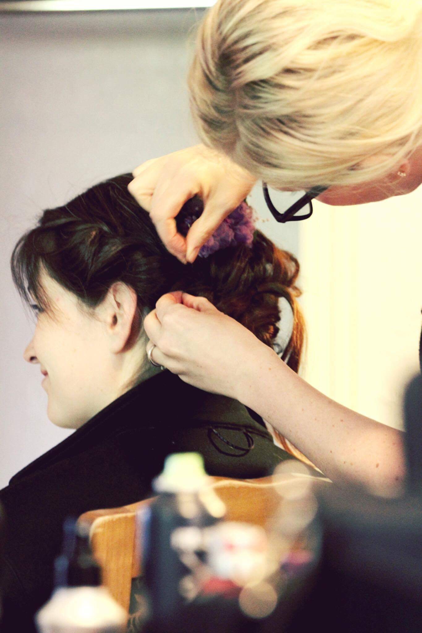 Bridal stylist securing a bride's updo and placing a floral hair accessory